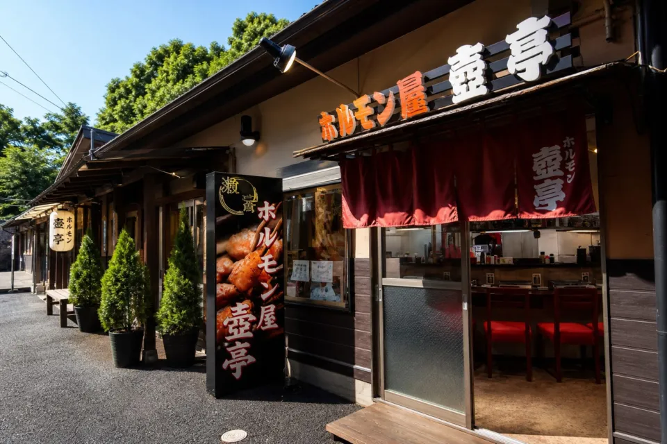 ホルモン屋 壺亭 東口屋台村店の夜に暖簾と看板が灯るホルモン屋 壺亭の外観