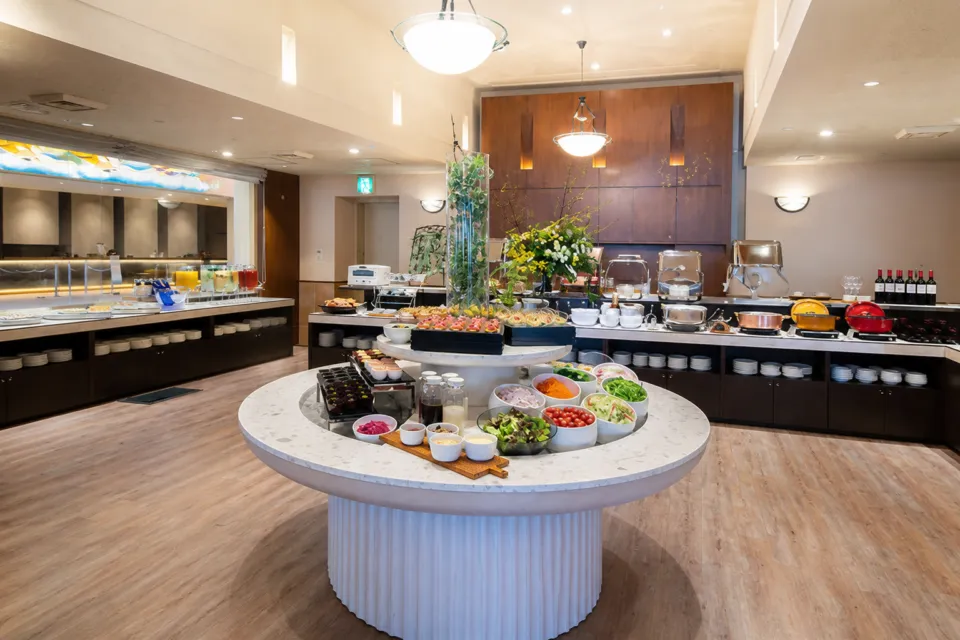 AOMORI BOLD KITCHENの中央の円形カウンターにサラダや料理が並ぶ明るいビュッフェ会場