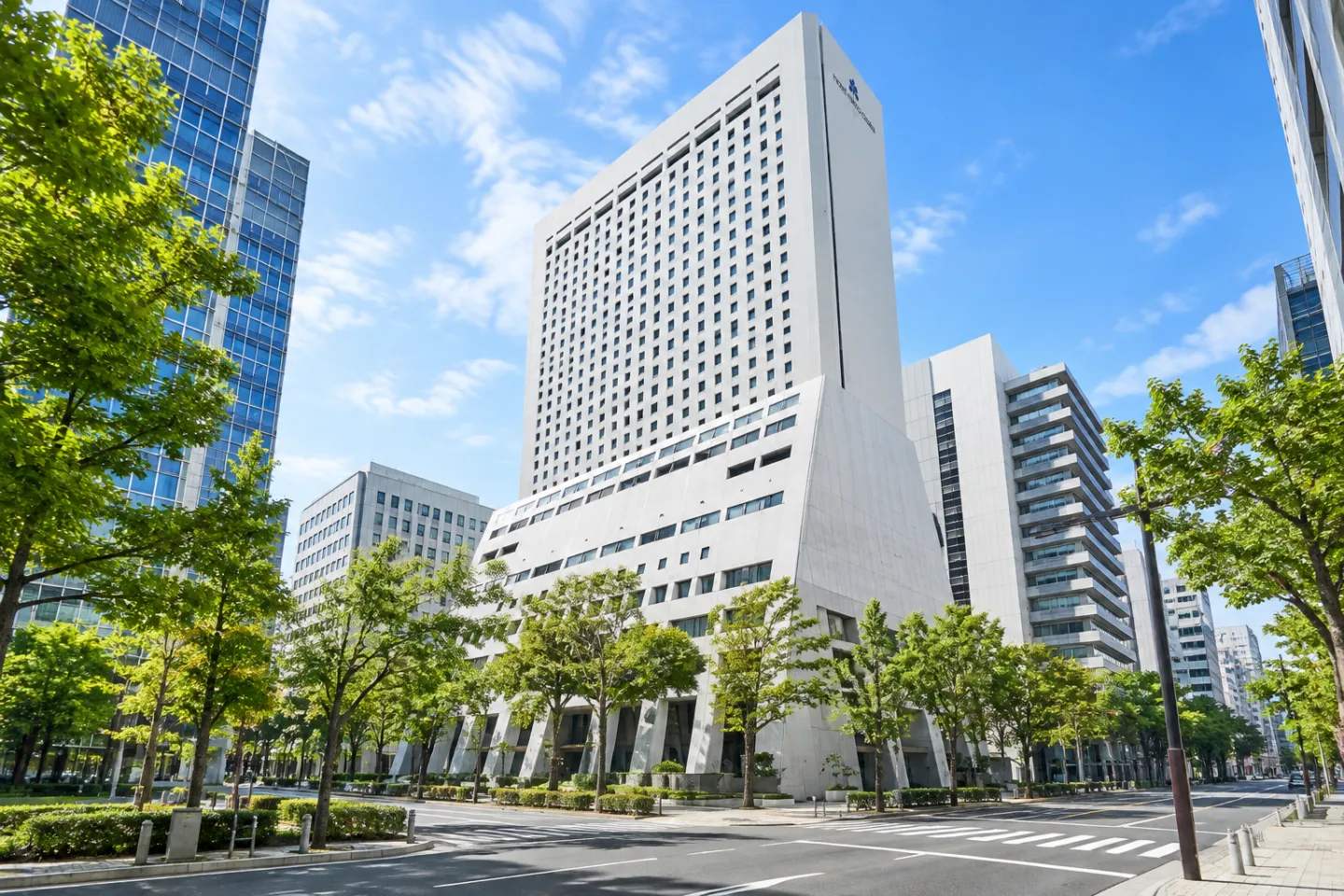 ホテル日航大阪の高層の白いホテル棟と街路樹が写る外観