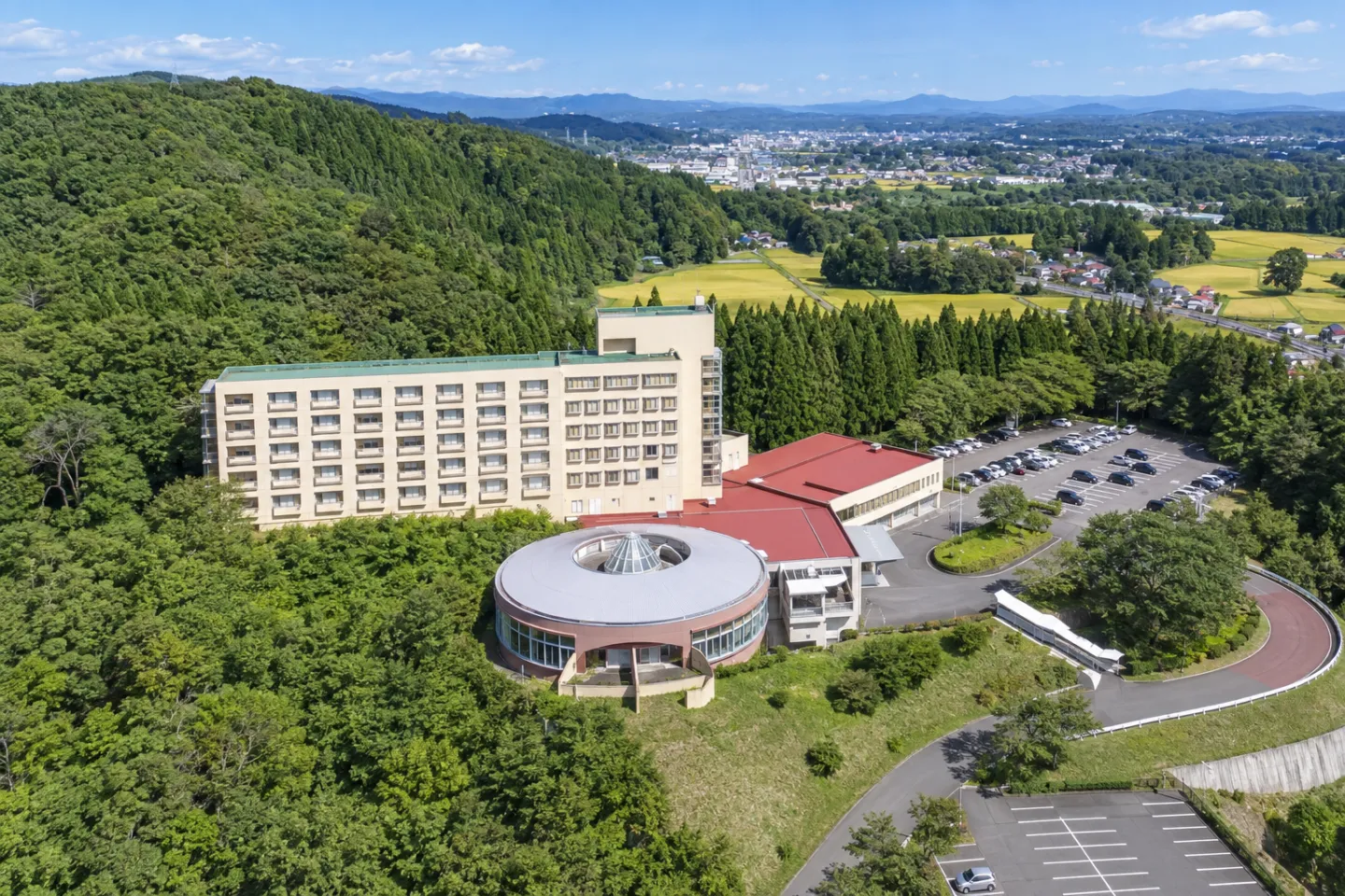 亀の井ホテル 一関の高台の建物全体と周囲の田園を見渡す外観