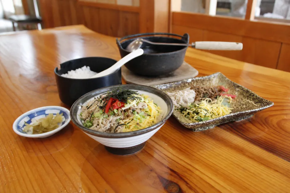 鶏飯の店 ひさ倉の木のテーブルに鶏飯の具材とだし、鶏料理が並ぶ食事風景