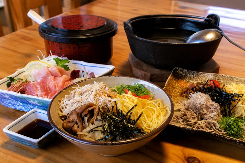 鶏飯の店 ひさ倉の鶏飯と鶏刺しを木のテーブルに並べたセット料理
