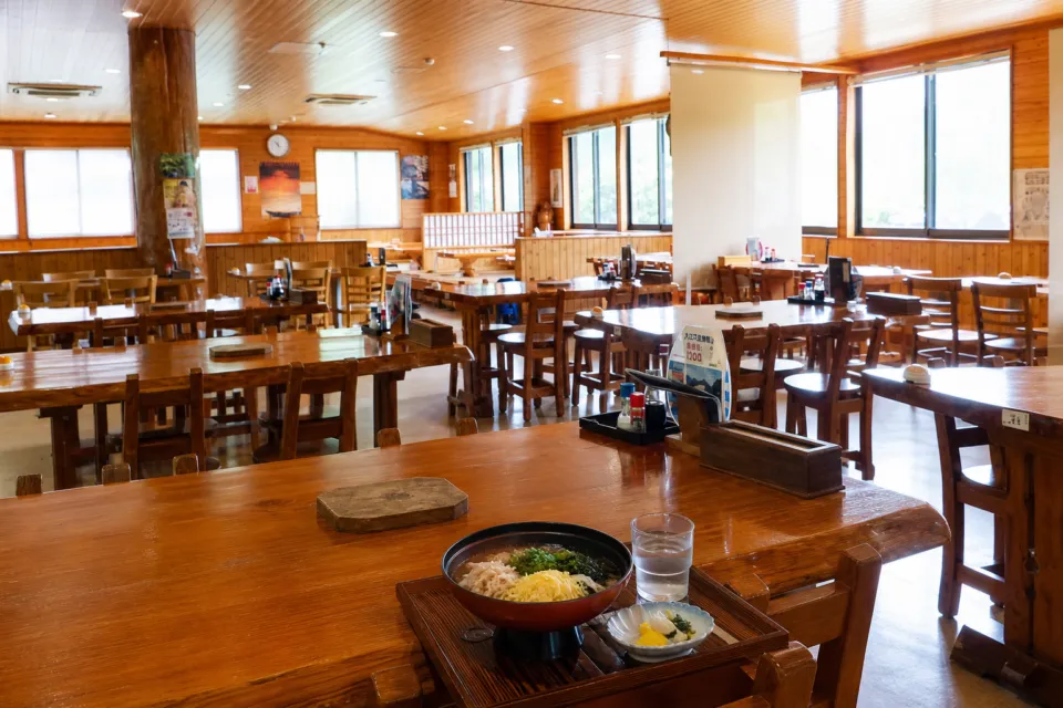 鶏飯の店 ひさ倉の大きな窓から光が入る木造のテーブル席