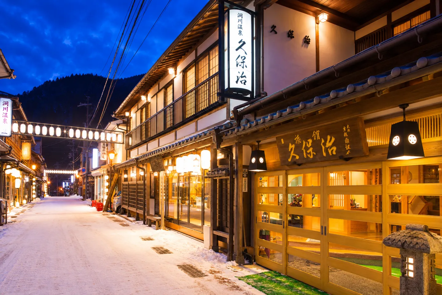 観光旅館 久保治の雪の温泉街に面した夜の外観