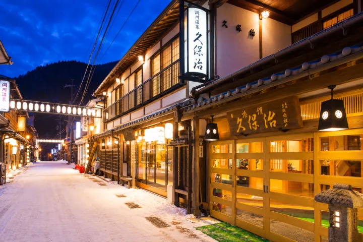 観光旅館 久保治の雪の温泉街に面した夜の外観