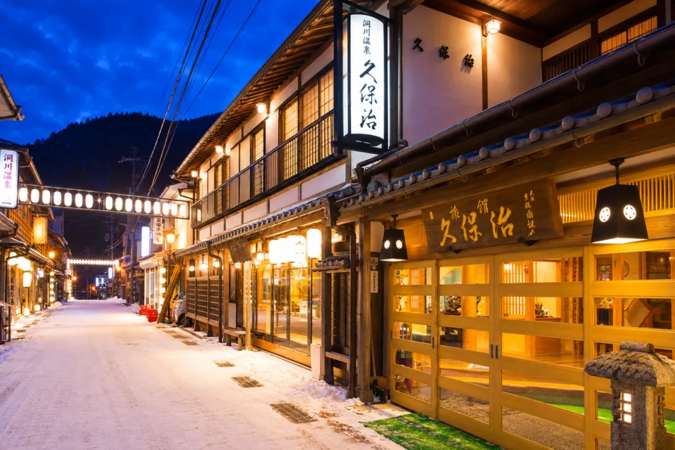 観光旅館 久保治の雪の温泉街に面した夜の外観