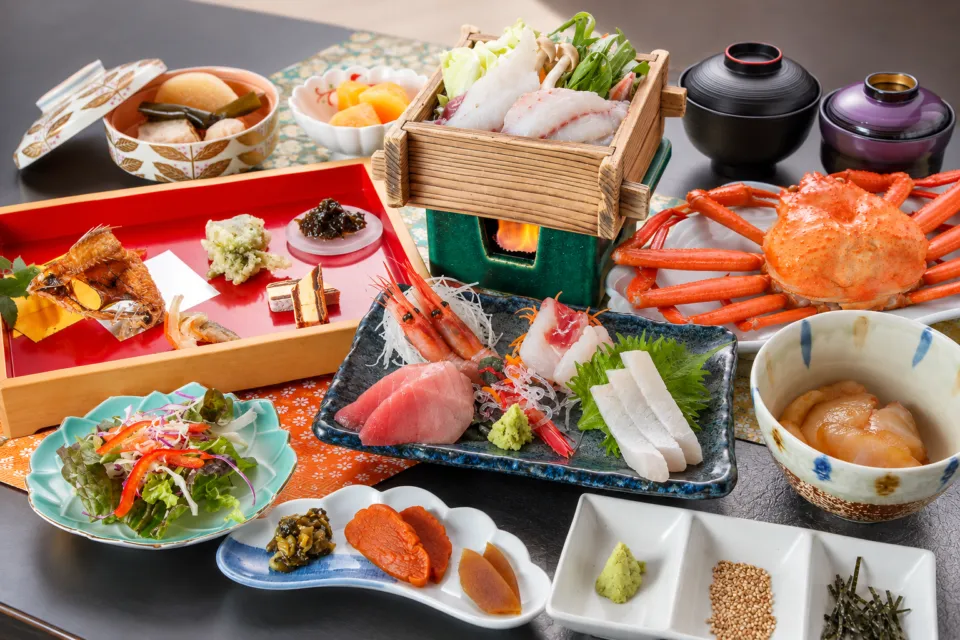 国際佐渡観光ホテル 八幡館のカニや刺身を並べた夕食の料理例