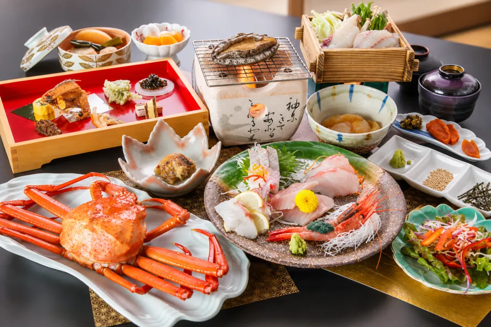 国際佐渡観光ホテル 八幡館の刺身やカニを配した夕食の料理例