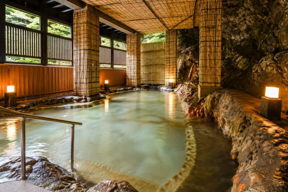 旅館 新明館の岩壁と竹の柱がある浴場