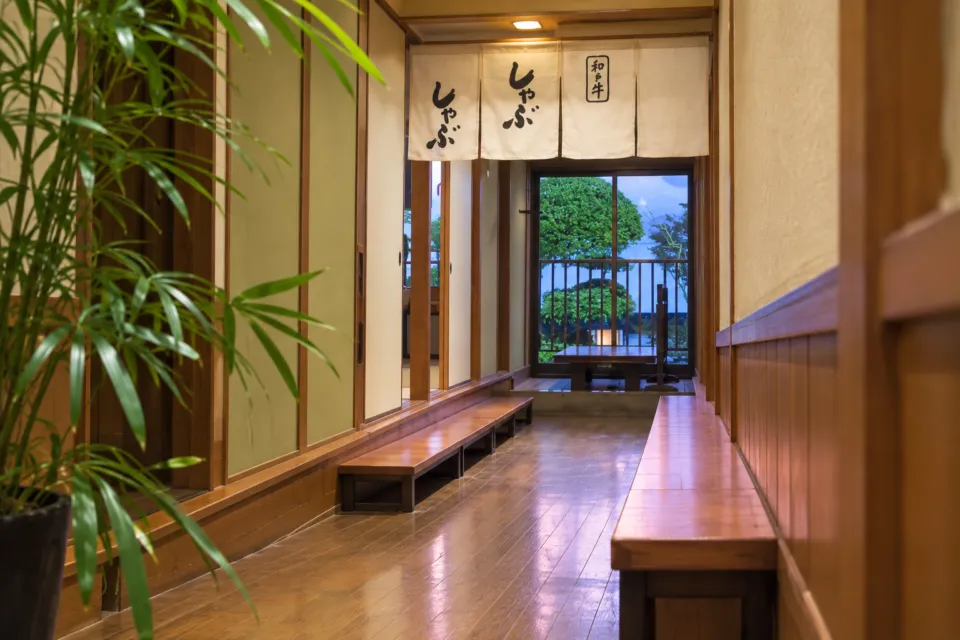 本家かもめ屋の暖簾と庭の緑が見える和風の廊下
