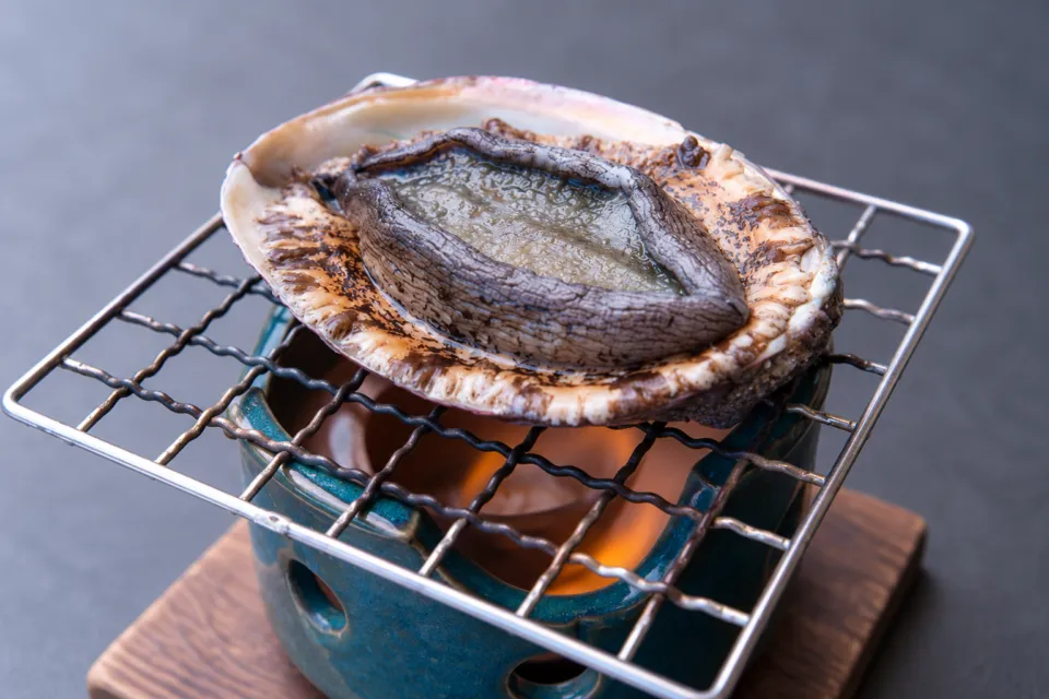 磯膳よしえいの網の上に置かれた殻付きアワビ
