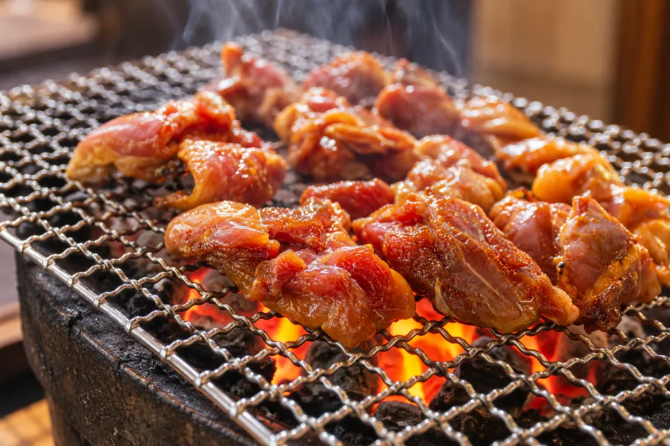 鶏炭火焼 らくだ山の網の上の鶏肉と赤く光る炭火
